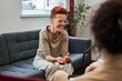 Woman laughing out loud while sitting at sofa and talking with her doctor during therapy