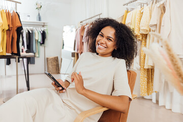 Wall Mural - Happy customer sitting in fashion store holding a smartphone and looking at camera