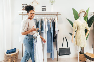 Woman working in a small fashion store, holding a bunch of hangers with clothes