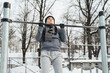Athletic woman doing pull-ups on horizontal bar during outdoor winter workout