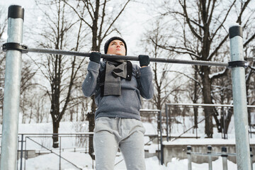 Wall Mural - Athletic woman doing pull-ups on horizontal bar during outdoor winter workout