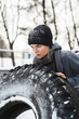 Athletic woman exercising with a tire during her workout at snowy and cold winter day
