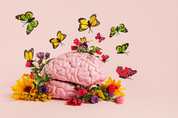 Human brain surrounded with various fresh flowers and butterflies on pastel pink background. Creative positive thinking or love concept. Minimal Mental Health Awareness idea. Spring flower bloom.