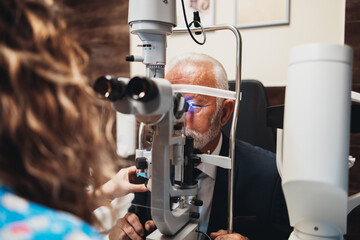 Wall Mural - Elegant senior bearded man receiving ophthalmology treatment. Doctor ophthalmologist checking his eyesight with modern equipment.