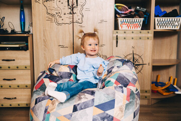 Portrait of a happy child, a little girl is sitting in a soft chair. Happy baby 1 year old.