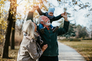 Happy good looking senior couple husband and wife walking and playing with their adorable grandson in public city park