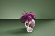 Day of The Dead skull adorned with purple flowers. On pastel dark green background with copy space