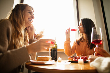 Wall Mural - Portrait of three beautiful women sitting at cafe, talking and drinking red wine. Weekend gathering