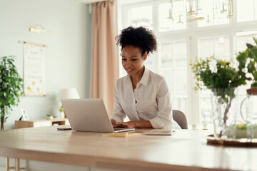 Wall Mural - A student surfs looking for information. The woman smiles and prints a message to the client by mail. The influencer works at home online on a computer. The hostess keeps a table on the Internet.