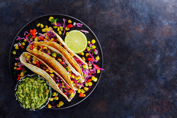 Vegetarian tacos with sweet corn, purple cabbage and tomatoes on a black plate. Tacos with vegetables and guacamole sauce on dark background. Copy space. Top view