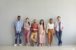 Portrait of a group of smiling multiracial people standing in a row on a light wall background. Diverse young men and women in casual clothes look at the camera. Concept of international friendship.