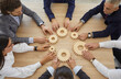 Team of businesspeople developing good business system. Group of senior and young business people sitting around table join gearwheels as metaphor for good effective teamwork. High angle, from above