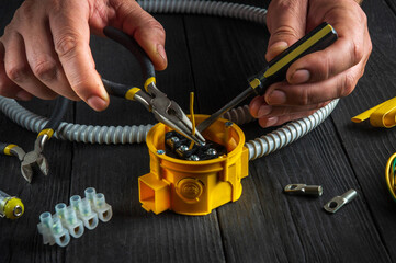 Installing a cable or wire to a junction box. Electrical connection in the workshop of professional master electrician. Close-up of hands of professional master electrician during work