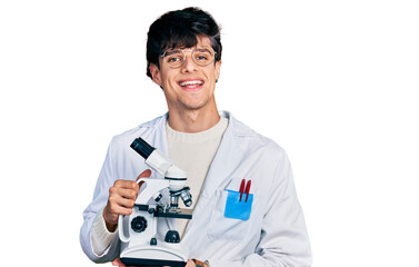 Poster - Handsome hipster young man wearing lab coat holding microscope smiling with a happy and cool smile on face. showing teeth.