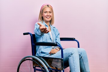 Poster - Beautiful blonde woman sitting on wheelchair smiling cheerful offering palm hand giving assistance and acceptance.