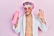 © Krakenimages.com - Young hispanic man wearing bathrobe and eye bags patches holding shampoo doing ok sign with fingers, smiling friendly gesturing excellent symbol