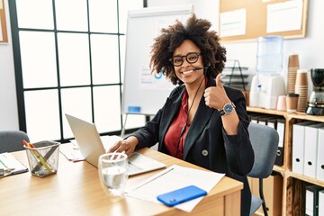 Canvas Print - African american woman with afro hair working at the office wearing operator headset doing happy thumbs up gesture with hand. approving expression looking at the camera showing success.