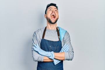 Poster - Young hispanic man wearing apron with arms crossed angry and mad screaming frustrated and furious, shouting with anger looking up.