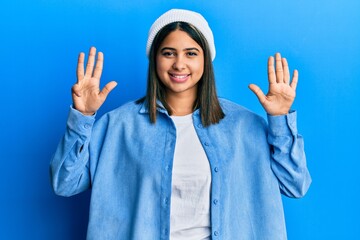 Poster - Young latin woman wearing cute wool cap showing and pointing up with fingers number nine while smiling confident and happy.