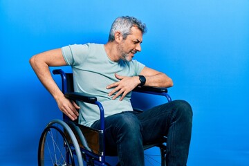 Poster - Handsome middle age man with grey hair sitting on wheelchair suffering of backache, touching back with hand, muscular pain