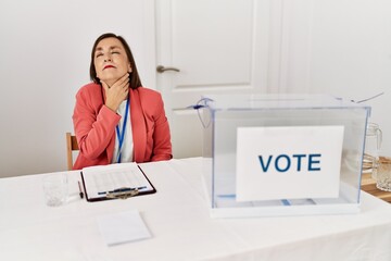 Canvas Print - Beautiful middle age hispanic woman at political election sitting by ballot touching painful neck, sore throat for flu, clod and infection