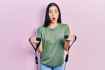 Poster - Beautiful woman with blue eyes training arm resistance with elastic arm bands afraid and shocked with surprise and amazed expression, fear and excited face.