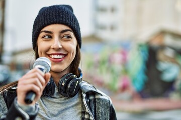 Wall Mural - Young hispanic woman smiling happy using headphones and microphone at the city.