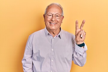 Wall Mural - Senior man with grey hair wearing elegant shirt and glasses smiling with happy face winking at the camera doing victory sign. number two.