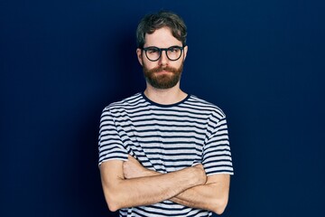 Wall Mural - Caucasian man with beard wearing striped t shirt and glasses skeptic and nervous, disapproving expression on face with crossed arms. negative person.