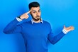 © Krakenimages.com - Young hispanic man with beard wearing casual blue sweater confused and annoyed with open palm showing copy space and pointing finger to forehead. think about it.