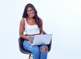 Poster - Young female in fashionable glasses sitting on a black chair with a laptop on her knees