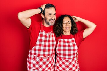 Wall Mural - Middle age couple of hispanic woman and man wearing cook apron smiling confident touching hair with hand up gesture, posing attractive and fashionable