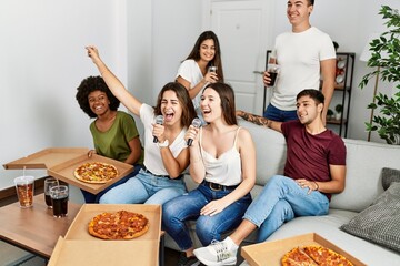 Wall Mural - Group of young friends having party eating italian pizza and singing song at home.