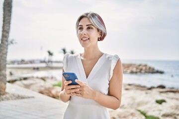 Poster - Young caucasian girl smiling happy using smartphone at the beach.