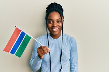 Poster - African american woman with braided hair holding gambia flag looking positive and happy standing and smiling with a confident smile showing teeth