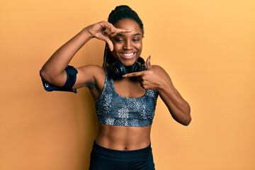 Poster - African american woman with braided hair wearing sportswear and arm band smiling making frame with hands and fingers with happy face. creativity and photography concept.