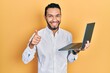 © Krakenimages.com - Hispanic man with beard working using computer laptop smiling happy and positive, thumb up doing excellent and approval sign