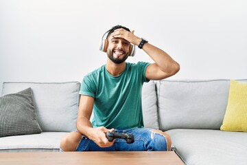 Sticker - Handsome hispanic man wearing headphones playing video game holding controller stressed and frustrated with hand on head, surprised and angry face