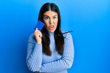 Canvas Print - Beautiful brunette woman holding credit card clueless and confused expression. doubt concept.