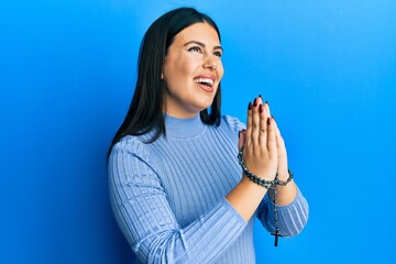 Wall Mural - Beautiful brunette woman praying holding catholic rosary smiling and laughing hard out loud because funny crazy joke.