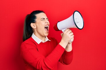 Wall Mural - Young brunette woman screaming through megaphone over isolated red background