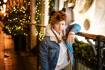 Young guy posing by the Christmas tree on the street in the evening, beautiful lights festive mood