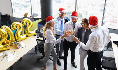 Wall Mural - Business people are celebrating holiday in modern office drinking champagne and having fun in coworking. Merry Christmas and Happy New Year 2022.