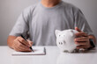 © ipuwadol - Business, finance, investment, financial planning, man hand touching piggy bank and writing note for planning, saving money, wealth and financial concept.
