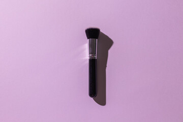 Wall Mural - Make-up brush on lilac background, top view. Cosmetics and beauty concept.