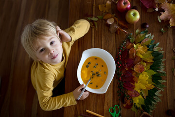 Wall Mural - Sweet child, boy, eating pumpkin soup, while applying leaves using glue while doing arts and chraft with leaves