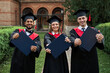 © Тарас Нагирняк - Group of three multinational students in graduation gowns female and male show diplomas to the camera