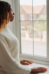 Beautiful young black elegant female leaning on the windowsill looking out of the window