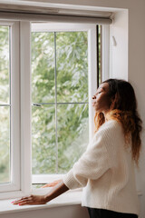 Beautiful young black elegant female leaning on the windowsill looking out of the window