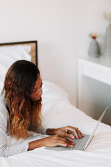 Canvas Print - Young beautiful black female on the bed working from home on her laptop